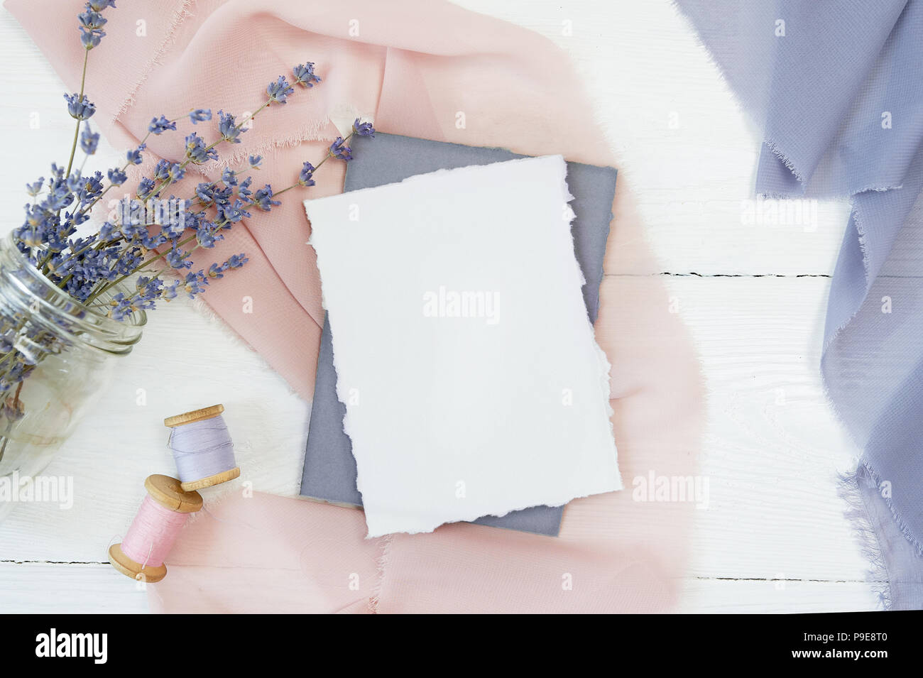 Carte vierge blanc sur fond de tissu bleu et rose avec des fleurs de lavande sur un fond blanc. Immersive avec enveloppe et carte vierge. Mise à plat. Vue d'en haut Banque D'Images