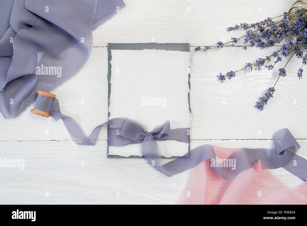 Carte vierge blanc ribbon bow sur fond de tissu bleu et rose avec des fleurs de lavande sur un fond blanc. Immersive avec enveloppe et carte vierge. Mise à plat. Vue d'en haut Banque D'Images