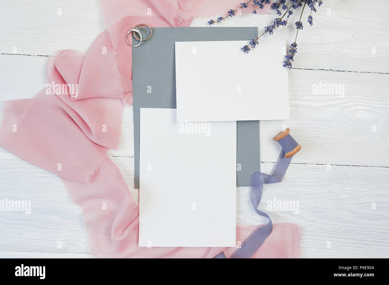 Carte vierge blanc avec des deux anneaux de mariage sur un fond de tissu rose et bleu avec des fleurs de lavande sur un fond blanc. Immersive avec enveloppe et carte vierge. Mise à plat. Vue d'en haut Banque D'Images