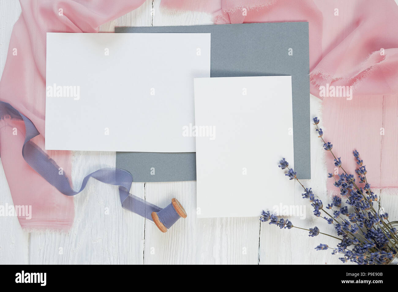 Carte vierge blanc ruban sur un fond de tissu rose et bleu avec des fleurs de lavande sur un fond blanc. Immersive avec enveloppe et carte vierge. Mise à plat. Vue d'en haut Banque D'Images