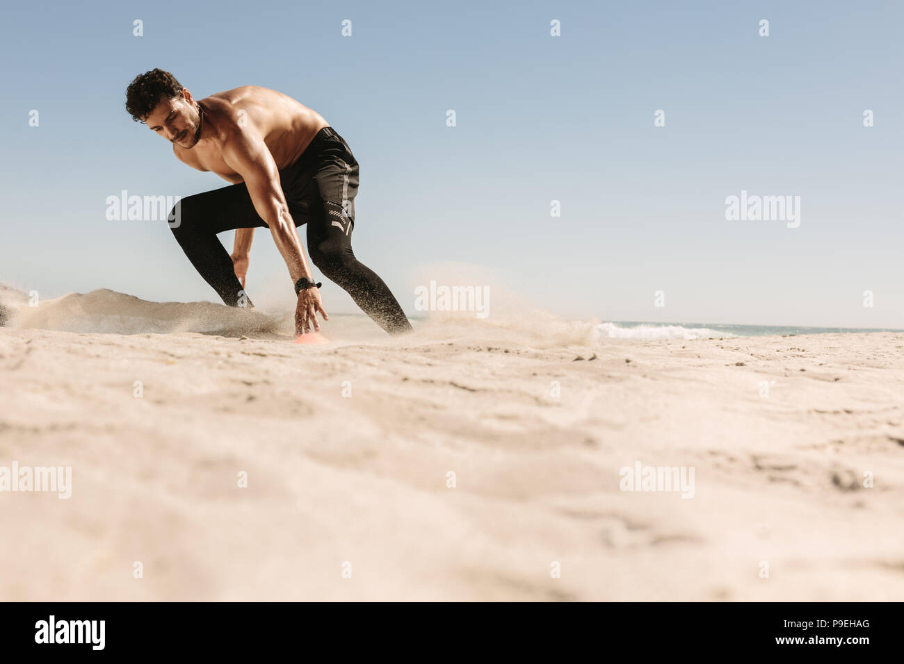 L'homme athlétique faible flexion à toucher la marque tout en courant sur la plage. L'homme de faire le travail de remise en forme à une plage sur une journée ensoleillée. Banque D'Images