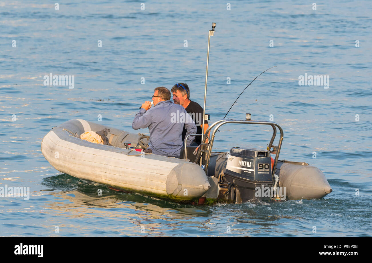 Paire d'hommes dans une côte avec un moteur hors-bord sur l'eau dans la soirée en été au Royaume-Uni. Banque D'Images