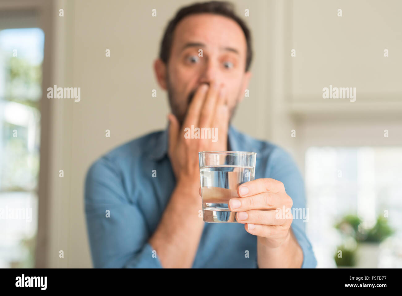 Homme d'âge moyen de boire un verre d'eau couvrir la bouche à part choqué avec honte pour erreur, expression de la peur, peur en silence, concept secret Banque D'Images