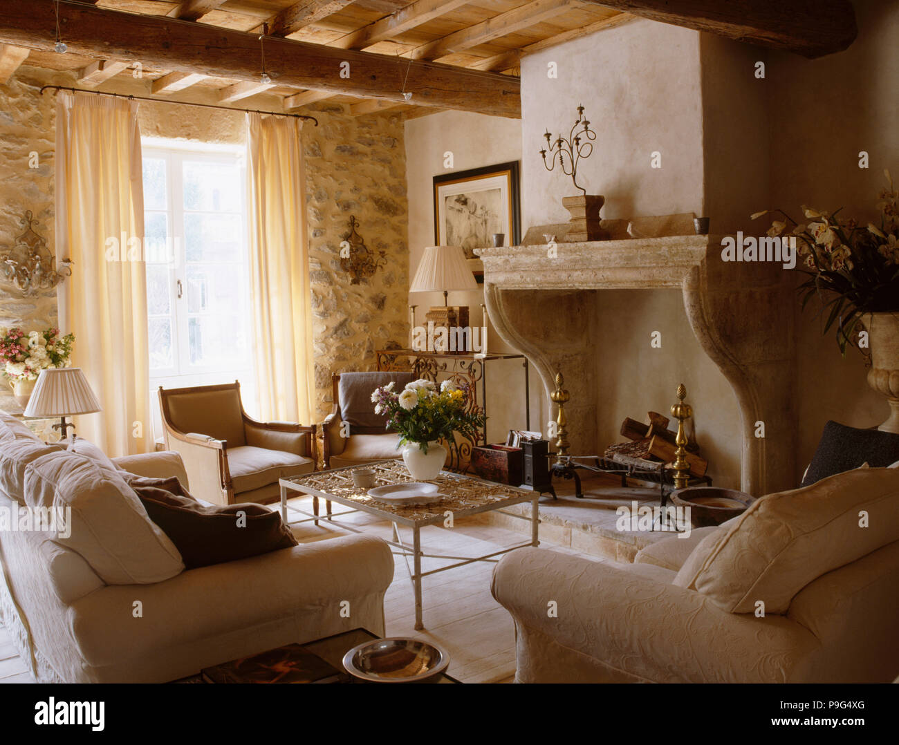 Les murs de pierre brute et grande cheminée en pierre dans le salon provençal avec de confortables fauteuils et canapé crème Banque D'Images