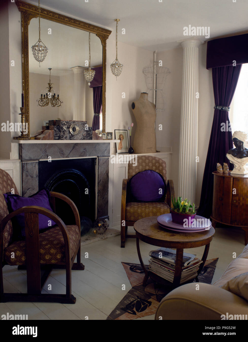 Chaises de style années 40 avec coussins violets dans un salon rétro avec un miroir antique au-dessus d'un effet cheminée en marbre Banque D'Images