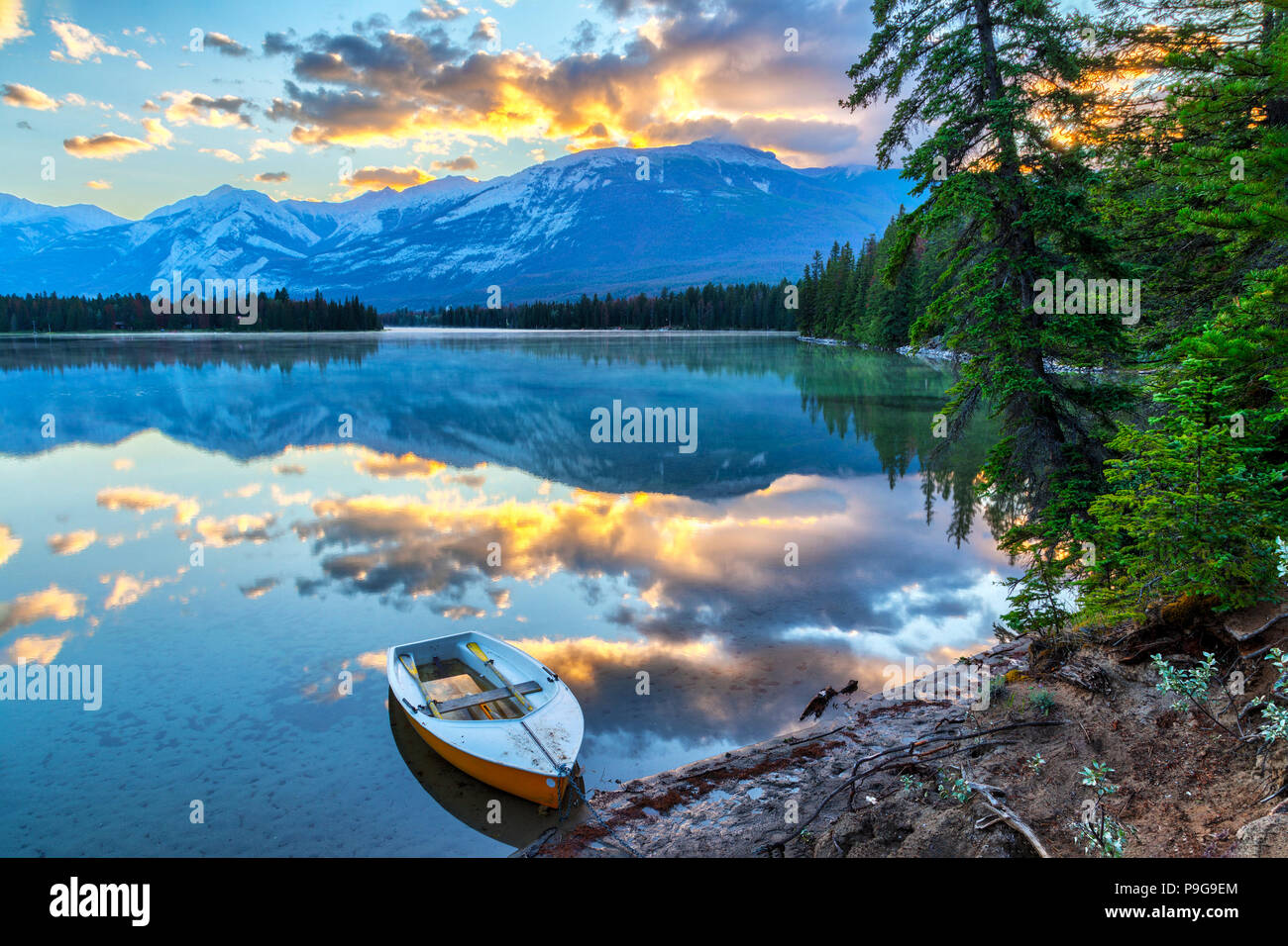 Soleil du matin éclate à travers les montagnes Rocheuses à Edith Lake dans le parc national Jasper, avec un bateau au premier plan. Banque D'Images
