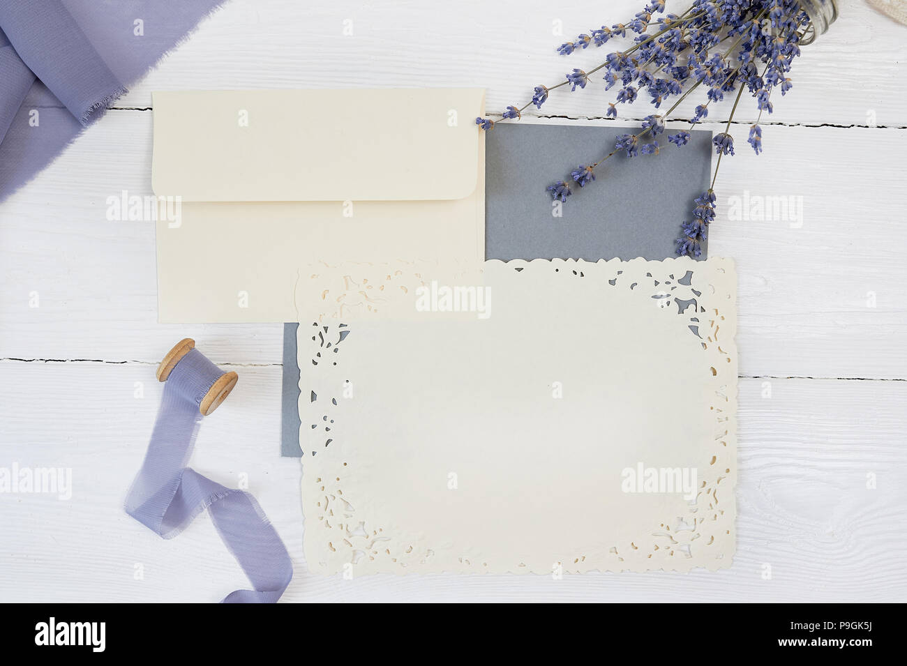 Carte vierge blanche, enveloppe et ruban sur fond de tissu bleu et rose avec des fleurs de lavande sur un fond blanc. Immersive avec enveloppe et carte vierge. Mise à plat. Vue d'en haut Banque D'Images