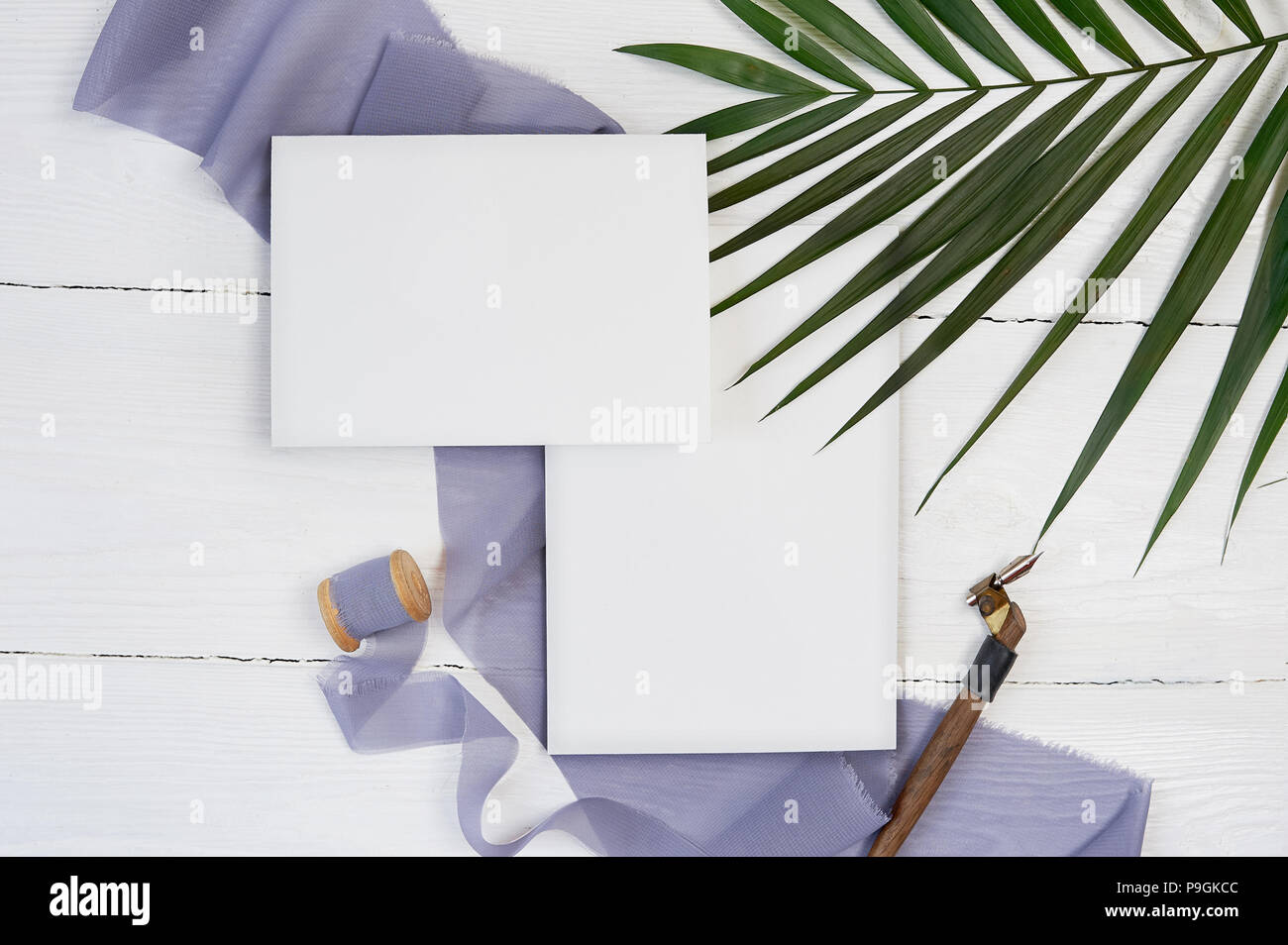 Carte de voeux vierge blanc ruban sur un fond de toile bleue avec la feuille de palmier et Plume calligraphique sur un fond blanc. Immersive avec enveloppe et carte vierge. Mise à plat. Vue d'en haut Banque D'Images