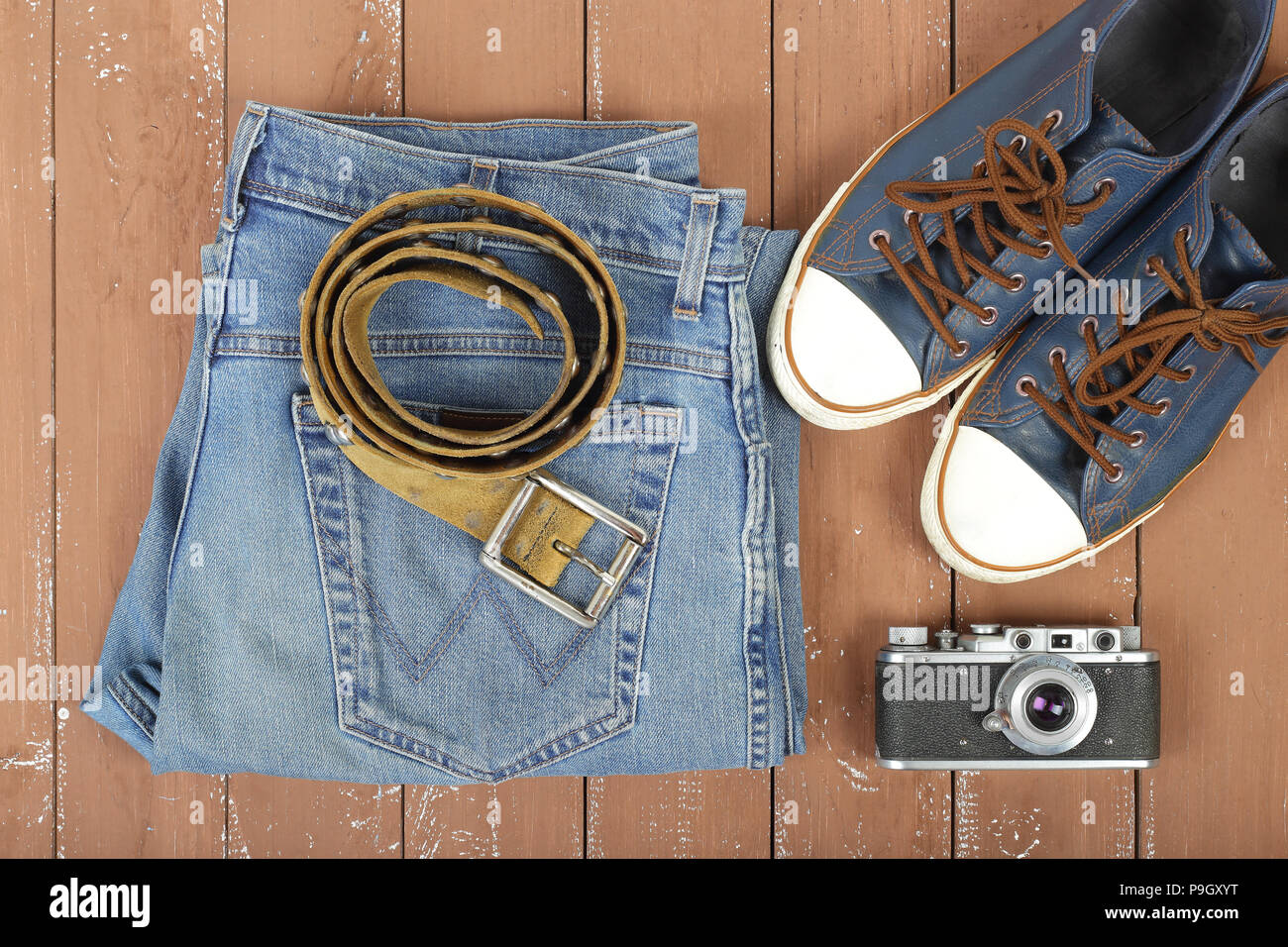 Vêtements, chaussures et accessoires - Top view la vieille caméra, ceinture de cuir, et gumshoes jeans bleu sur un fond de bois Banque D'Images