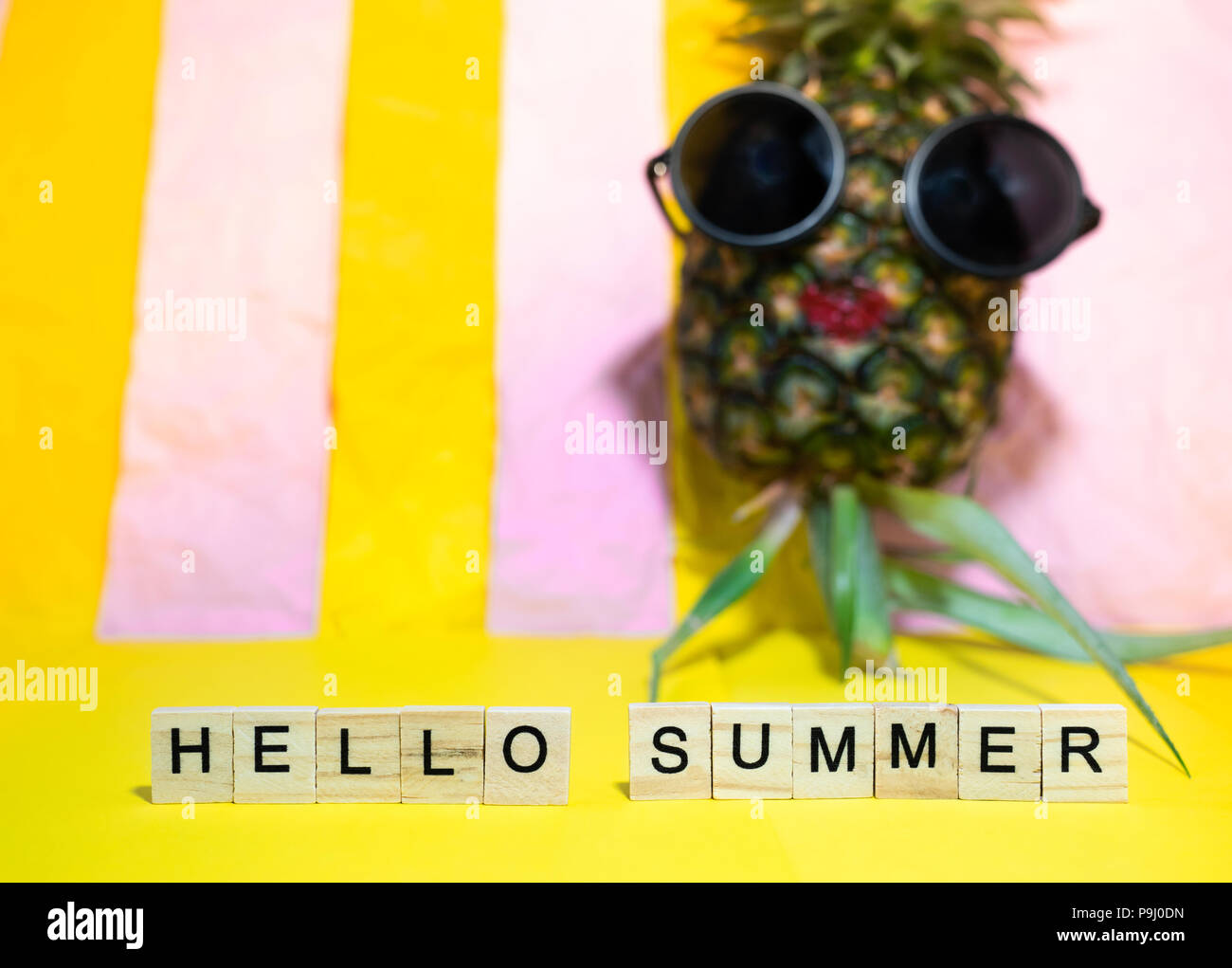 Cubes en bois avec des mots écrits Hello summer et lèvre rouge porte des lunettes d'ananas, bain de soleil sur un jaune vif et rose stripe pastel backgroun Banque D'Images