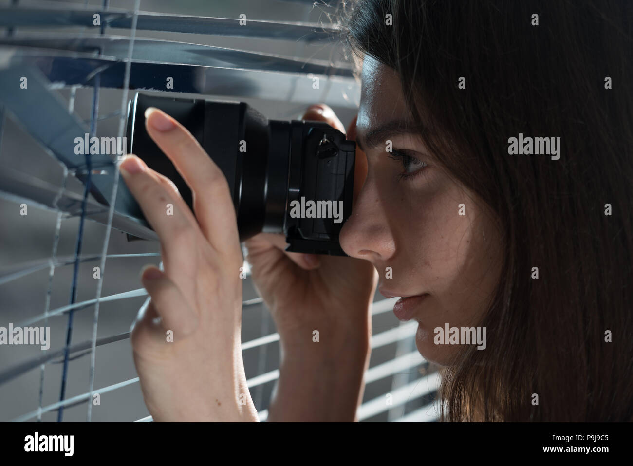 Jeune femme Paparazzi prendre une photo d'un air suspicieux autour d'un abat-jour tout en utilisant un appareil photo. Concept PIBR Banque D'Images