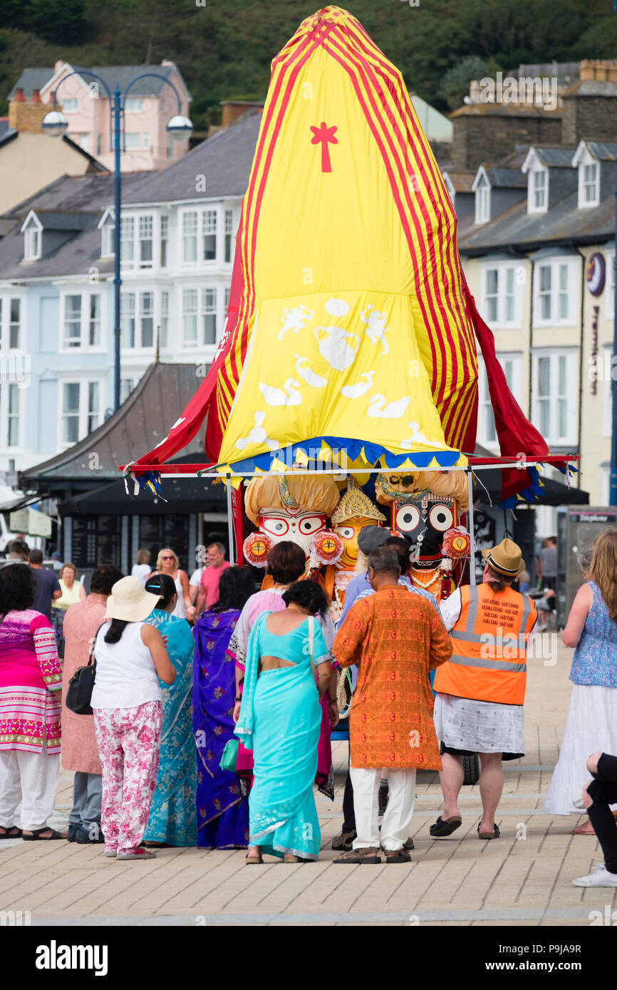 La foi et la religion sur le Royaume-uni : un groupe de dévots Hare Krishna avec leur "Ratha' un temple mobile votive char pour la déité Seigneur Jagannath, chantant comme ils le remorquer le long de la promenade à Aberystwyth, Pays de Galles, Royaume-Uni par un après-midi d'été Banque D'Images