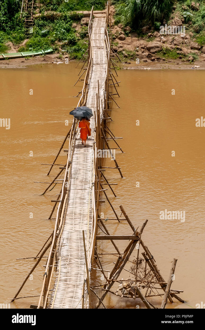 Les moines bouddhistes, traverser la rivière Nam Khan sur un pont de bambou, se protégeant du soleil avec des parasols à Luang Prabang, Laos Banque D'Images