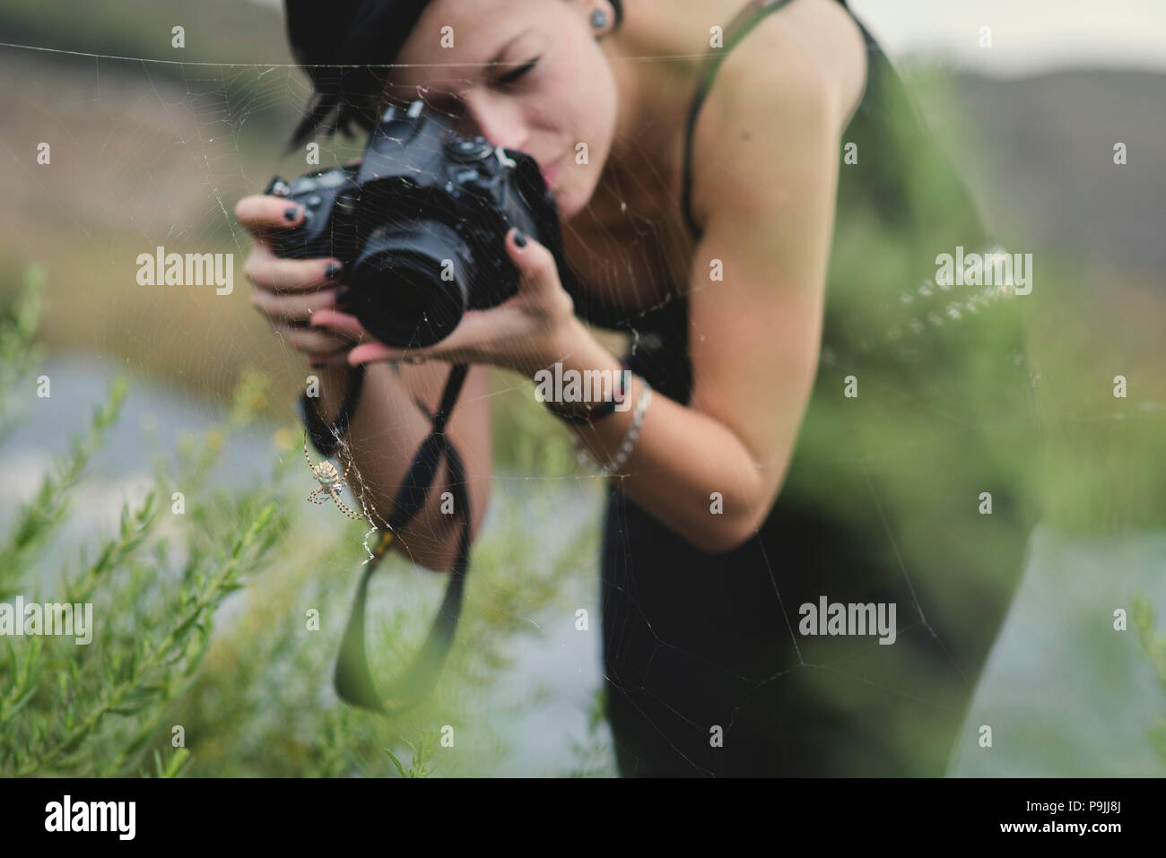 Belle jeune femme photographe portant des vêtements noirs de prendre des photos macro de la nature et des insectes à l'extérieur. Tiger araignée dans sa toile d'araignée étant phot Banque D'Images