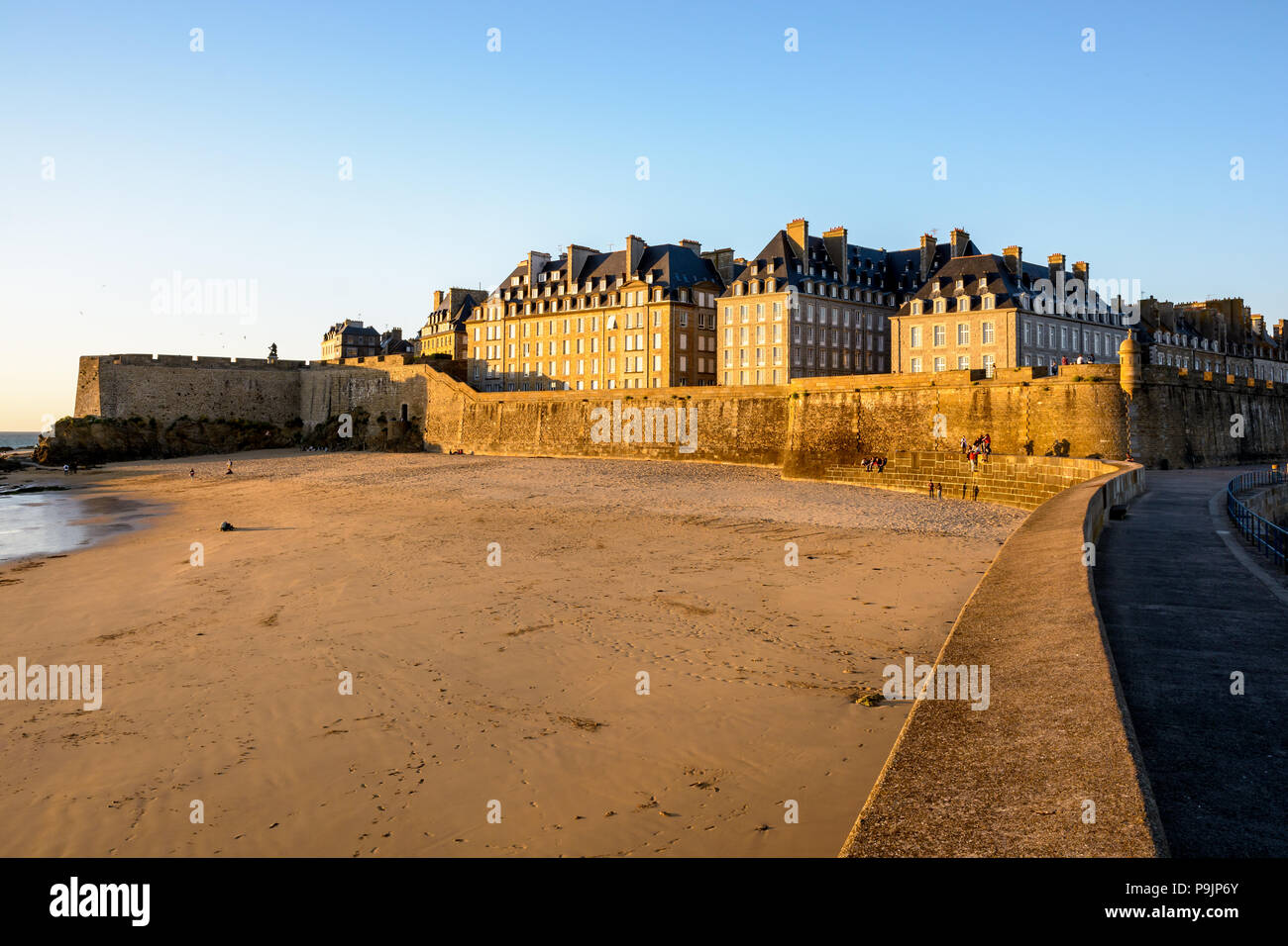 La ville fortifiée de Saint-Malo au coucher du soleil avec des bâtiments baignés de lumière chaude dépassant le mur et la Mole beach au pied des remparts. Banque D'Images La ville fortifiée de Saint-Malo au coucher du soleil avec des bâtiments baignés de lumière chaude dépassant le mur et la Mole beach au pied des remparts. Banque D'Images