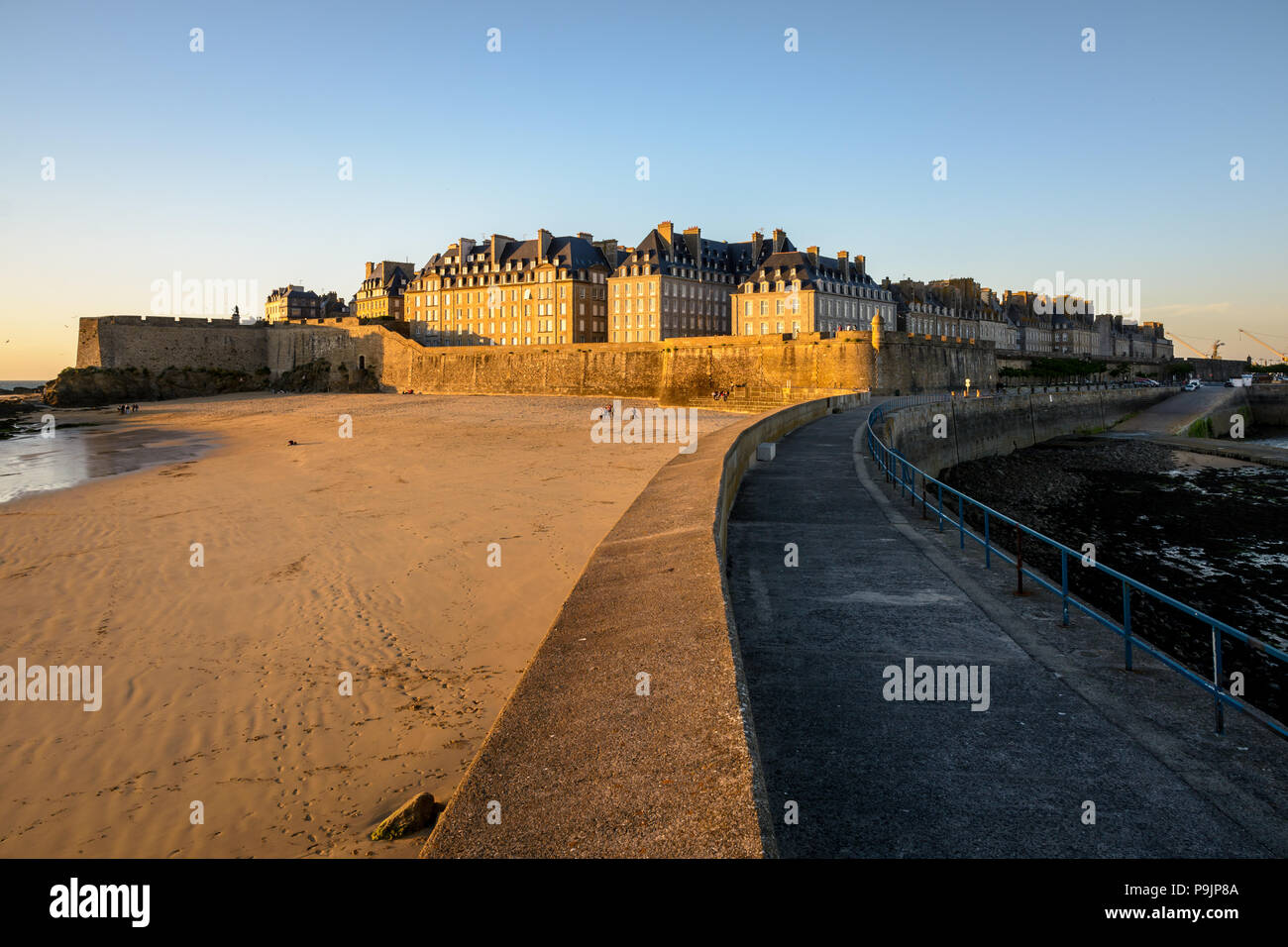 La ville fortifiée de Saint-Malo au coucher du soleil avec des bâtiments baignés de lumière chaude dépassant le mur et la Mole beach au pied des remparts. Banque D'Images La ville fortifiée de Saint-Malo au coucher du soleil avec des bâtiments baignés de lumière chaude dépassant le mur et la Mole beach au pied des remparts. Banque D'Images