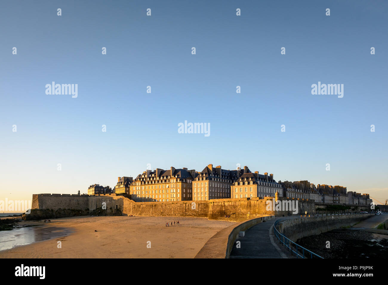 La ville fortifiée de Saint-Malo au coucher du soleil avec des bâtiments baignés de lumière chaude dépassant le mur et la Mole beach au pied des remparts. Banque D'Images