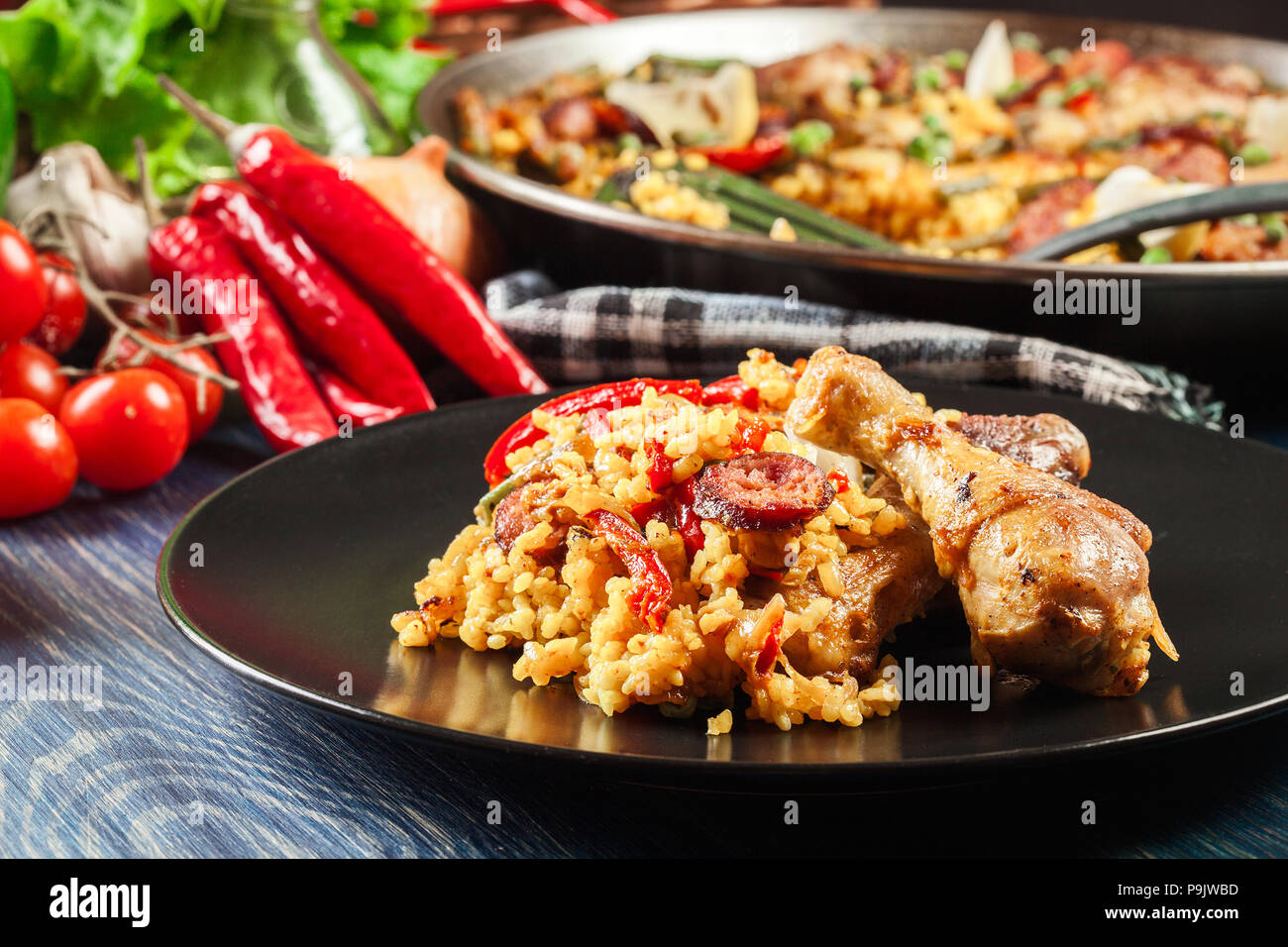 La paella traditionnelle avec des cuisses de poulet, saucisses chorizo et légumes servi sur la plaque noire. La cuisine espagnole Banque D'Images