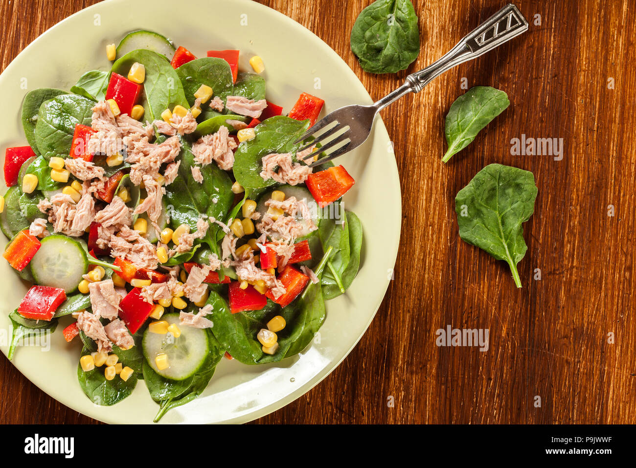 Salade d'épinards frais avec du thon, concombre, maïs, et paprika rouge sur une assiette. Matières premières alimentaires sains concept. Vue d'en haut Banque D'Images