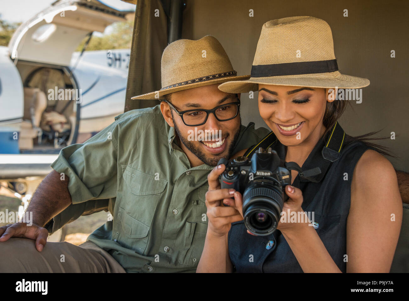 Couple de touristes en safari visualisation des photos sur l'appareil photo, avec un Pilatus PC12 de l'aviation côtière en Tanzanie en arrière-plan. Banque D'Images