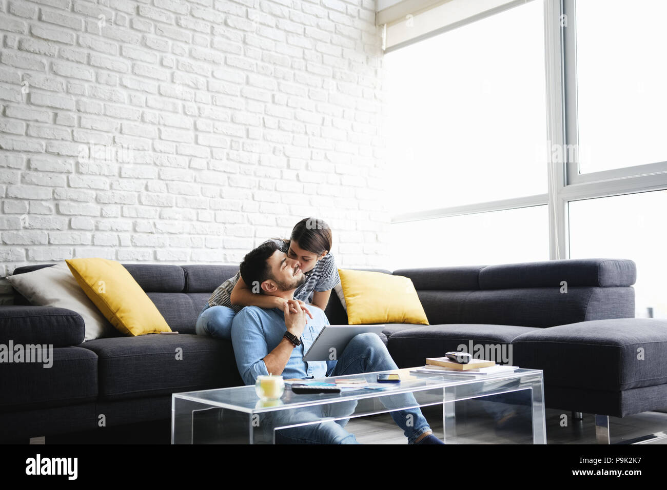 Young hispanic couple sitting on sofa at home, à l'aide d'un tablet PC pour Internet et les médias sociaux. La fille est serrant son petit ami et sourit à huis clos Banque D'Images