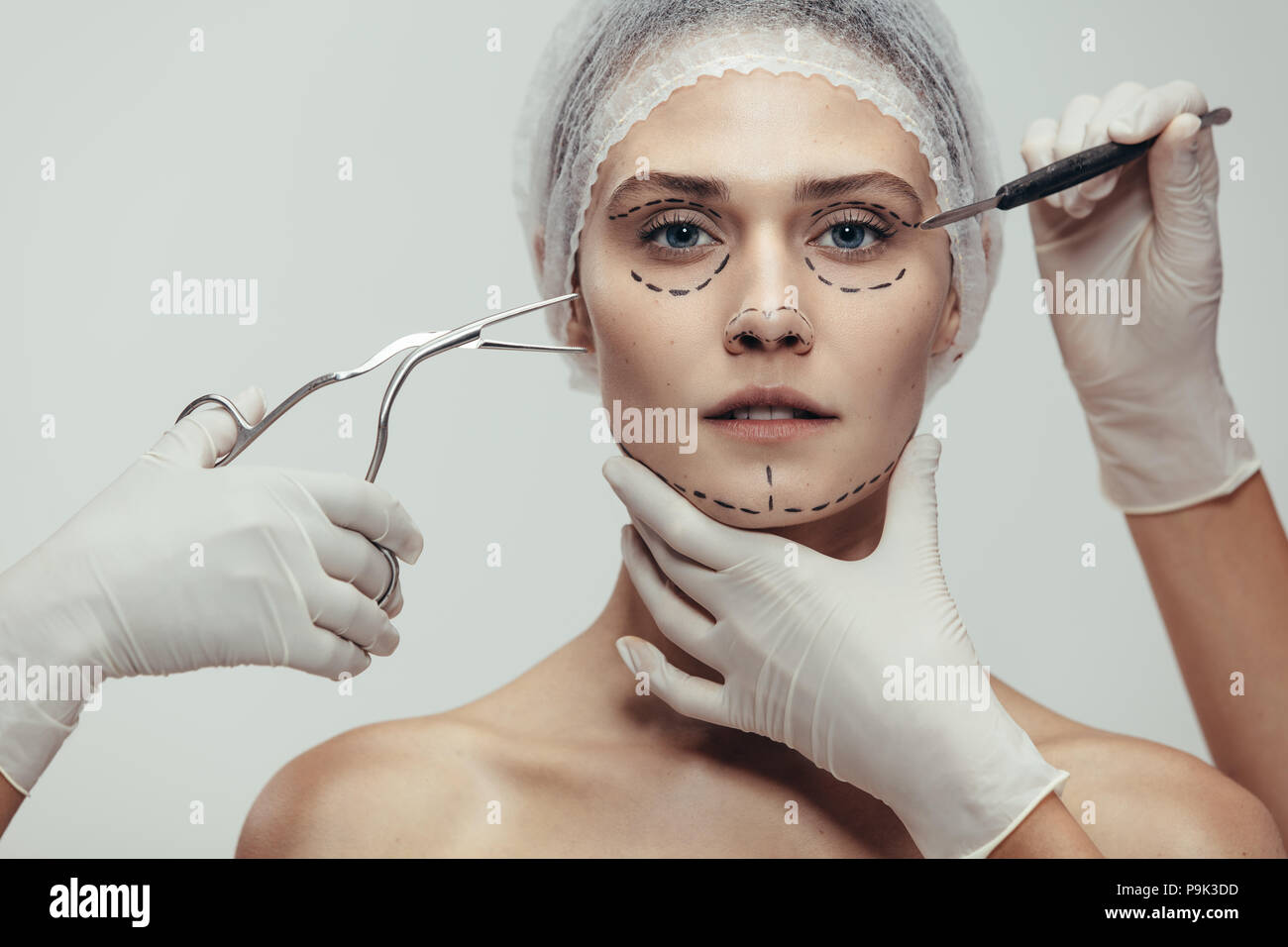 Close up of woman's face à la chirurgie esthétique et médicale scalpel contre forceps fond gris. Une femme qui lutte contre le vieillissement et l'ascenseur de visage surge Banque D'Images