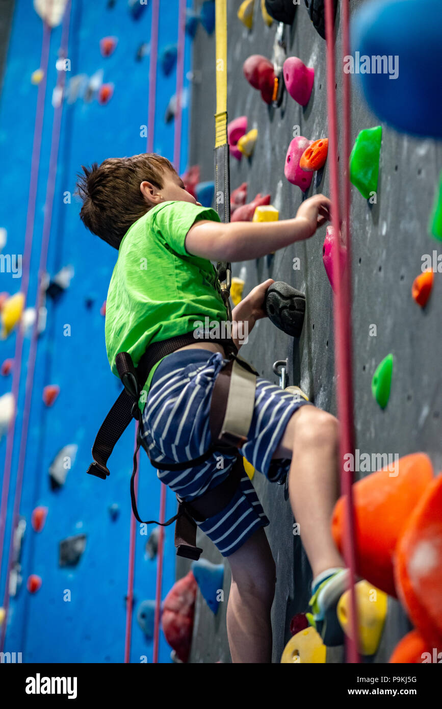 Jeune garçon grimper sur la paroi intérieure de la pratique rock gym Banque D'Images