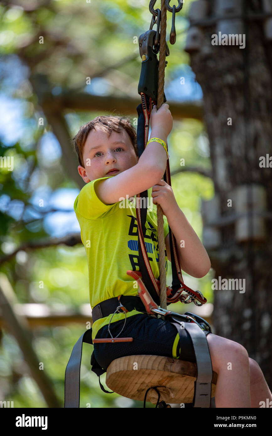 Portrait d'un beau garçon sur une corde entre les arbres du parc. Activités d'été pour enfants. Banque D'Images