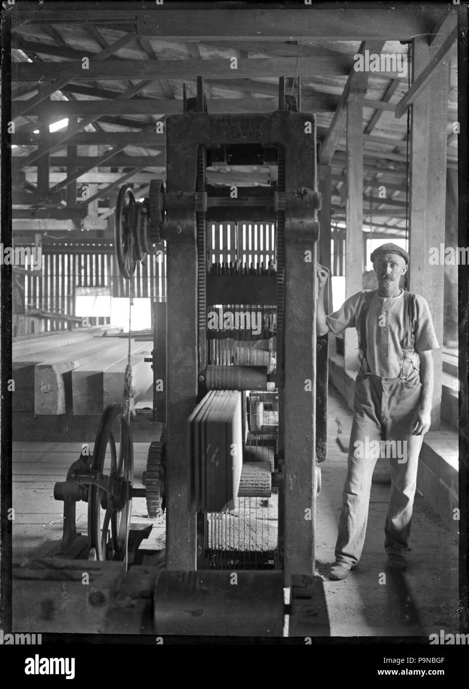 Travailleur 333 debout à côté de machines pour les planches à découper dans une scierie ATLIB 239804 Banque D'Images