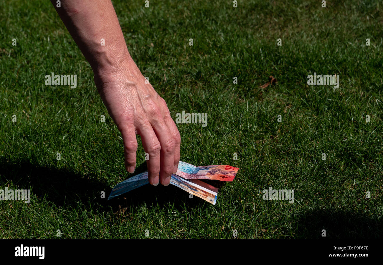 Cueillette à la main de l'argent à partir du sol. la monnaie suisse Swiss francs au sol d'herbe. Banque D'Images