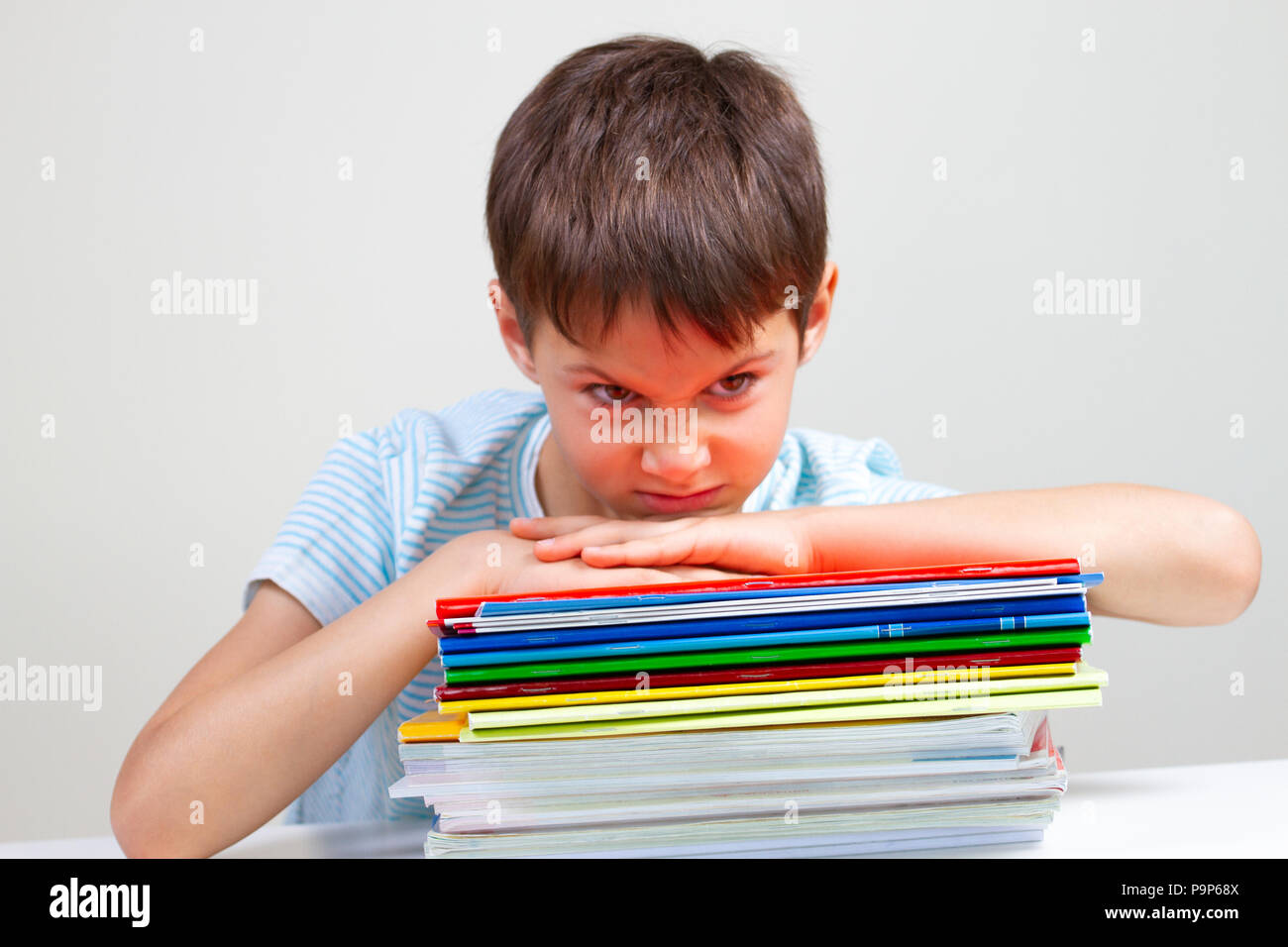 Écolier en colère sitting at desk with pile de livres et cahiers scolaires Banque D'Images