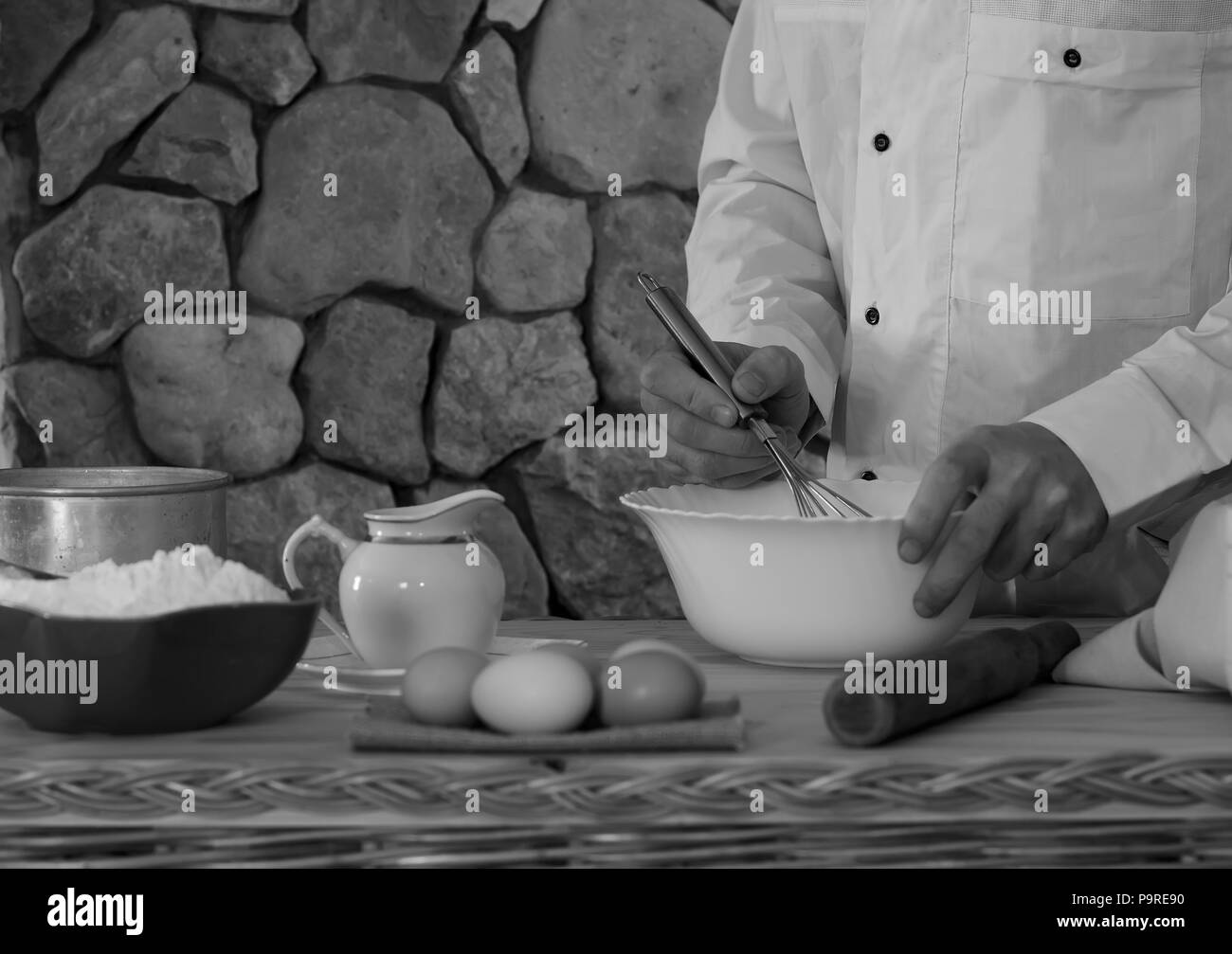 Bol avec la farine, des œufs, un tamis et un mortier, un homme et faire cuire dans un vêtement blanc battez les fouetter la pâte. Concept de cuisine rustique, selective focus Banque D'Images