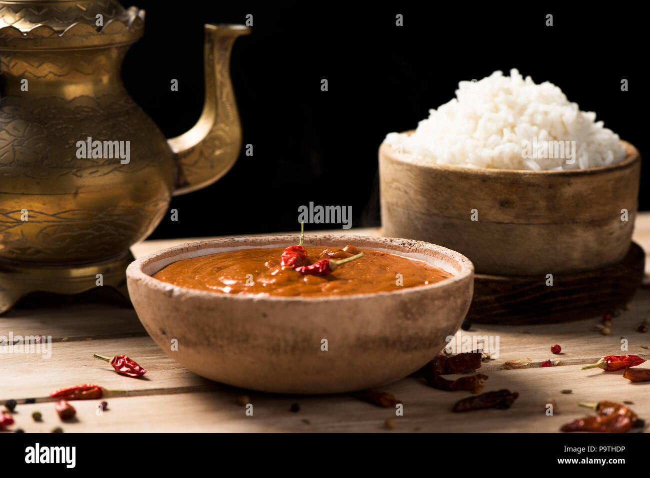 Libre d'un bol avec un poulet korma curry, un bol avec du riz cuit et une théière d'or sur une table en bois blanc, sur un fond noir Banque D'Images