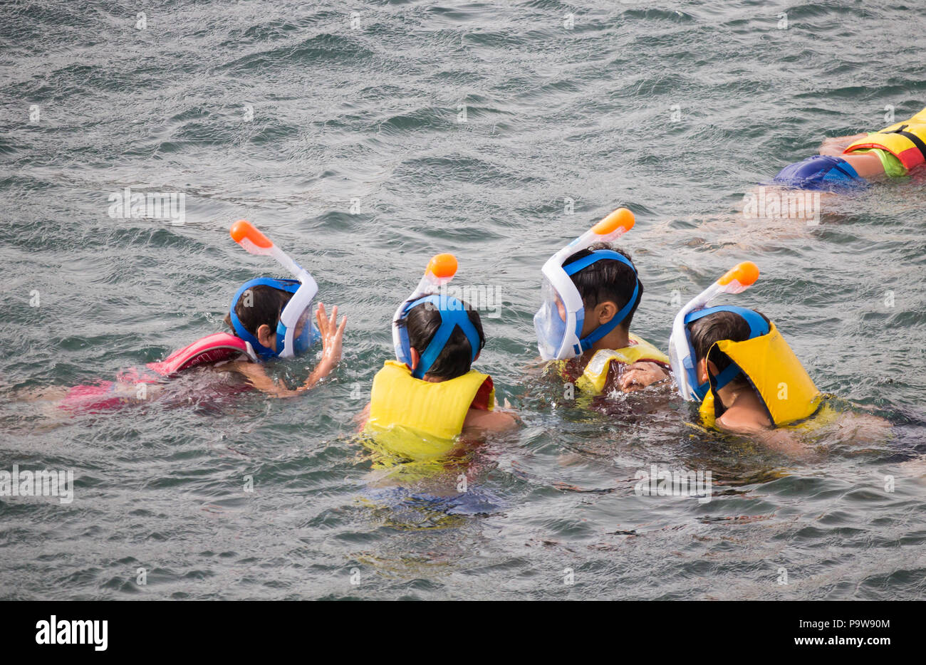 Aides à la flottabilité des enfants portant des masques faciaux avec tuba dans la mer. Banque D'Images