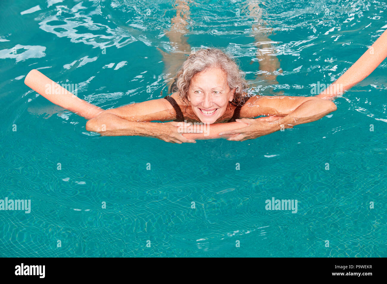 Smiling senior femme dans la piscine est en train de faire avec l'aide de la flottabilité aqua fitness Banque D'Images