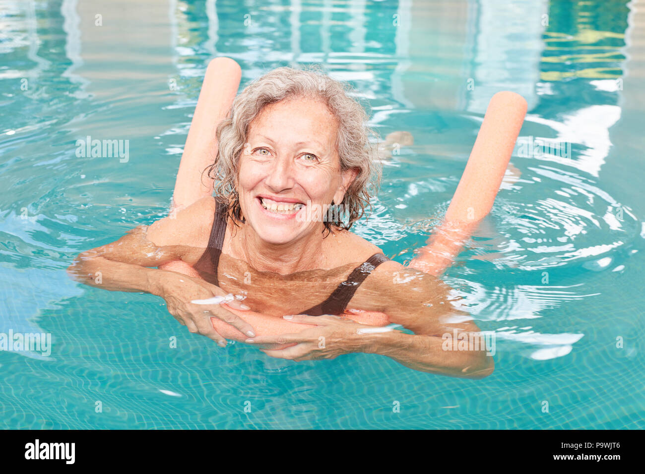 Senior Vital femme apprend à nager dans la piscine en nageant et nouilles Banque D'Images