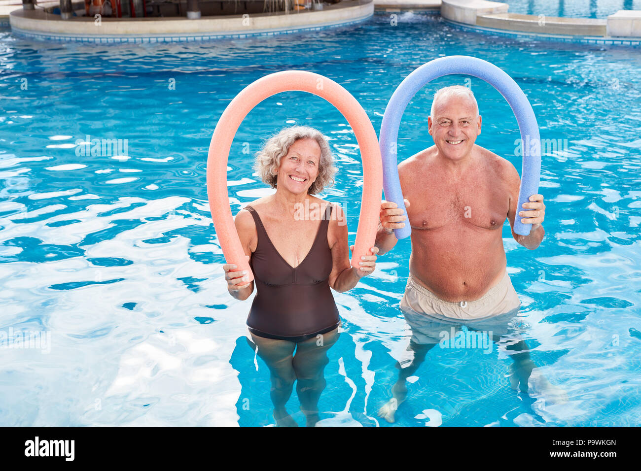 Professionnels Seniors couple avec nouilles de natation dans la piscine de l'hôtel Banque D'Images