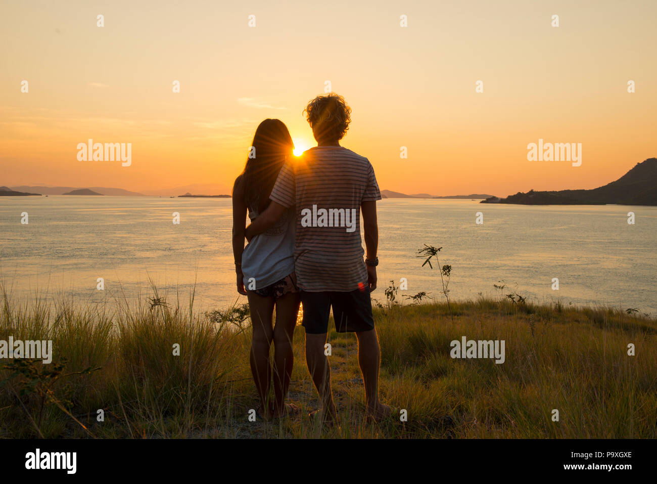 Un jeune couple de touristes debout sur un promontoire donnant sur le magnifique coucher de soleil sur le Parc National de Komodo, en Indonésie. Banque D'Images