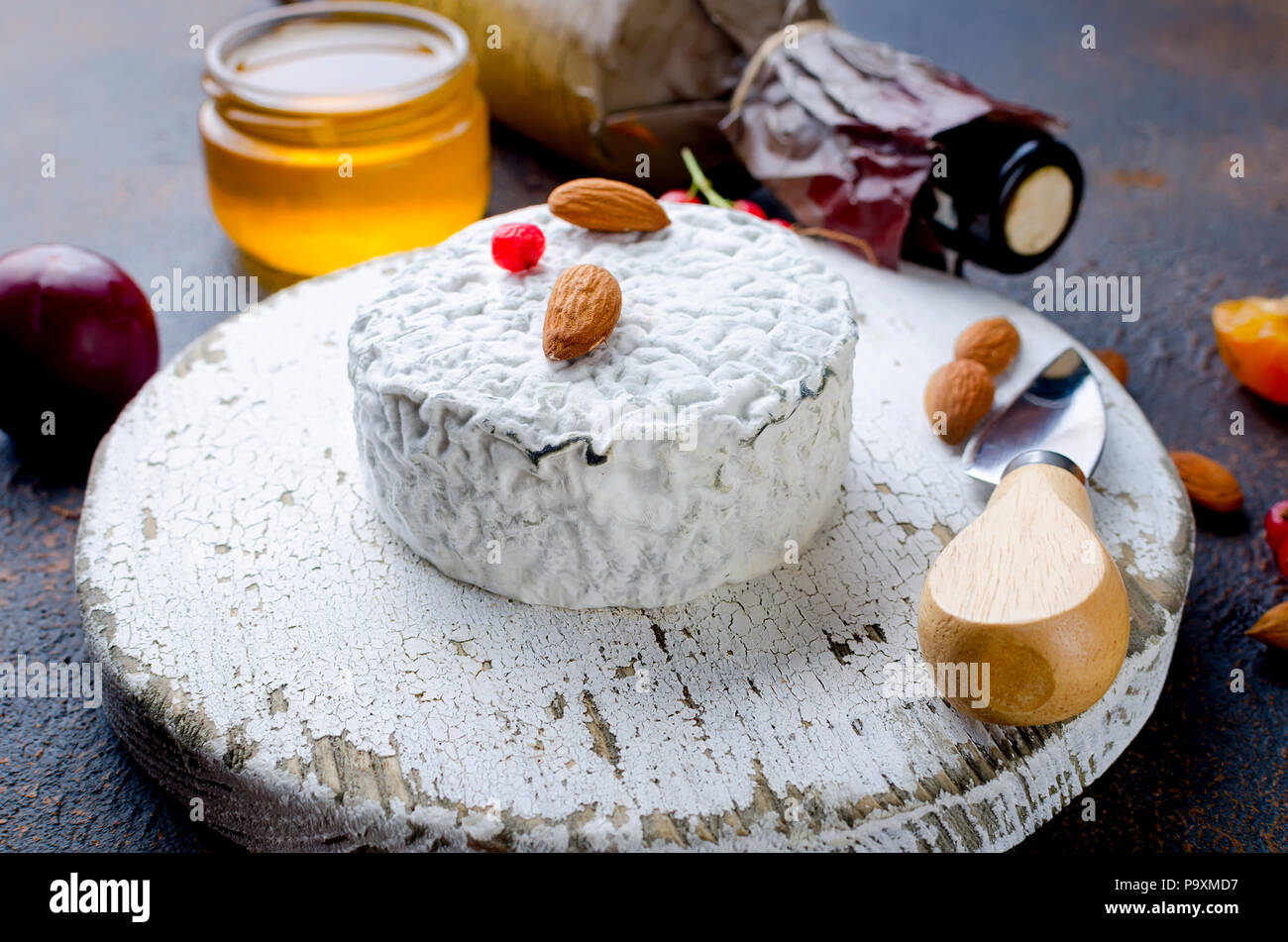 Tête ronde de fromage bleu avec du miel, de cassis, de fruits à coque et une bouteille de vin sur un tableau sombre, concept de gastronomie, fromage italien, romantique ev Banque D'Images