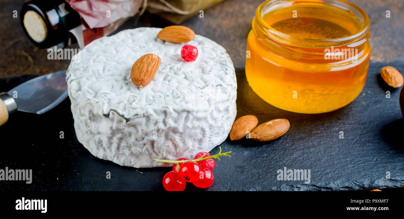 Tête ronde de fromage bleu avec du miel, de cassis, de fruits à coque et une bouteille de vin sur un tableau sombre, concept de gastronomie, fromage italien, romantique ev Banque D'Images