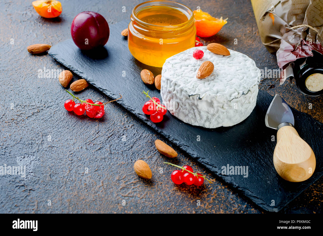 Tête ronde de fromage bleu avec du miel, de cassis, de fruits à coque et une bouteille de vin sur un tableau sombre, concept de gastronomie, fromage italien, romantique ev Banque D'Images