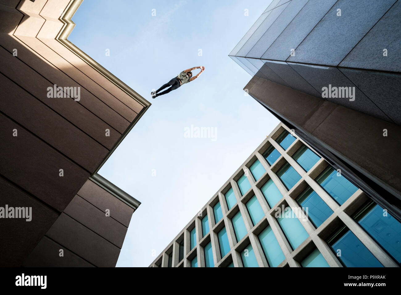 Vue de dessous du parkour masculin athlète sautant d'un toit à un autre Banque D'Images