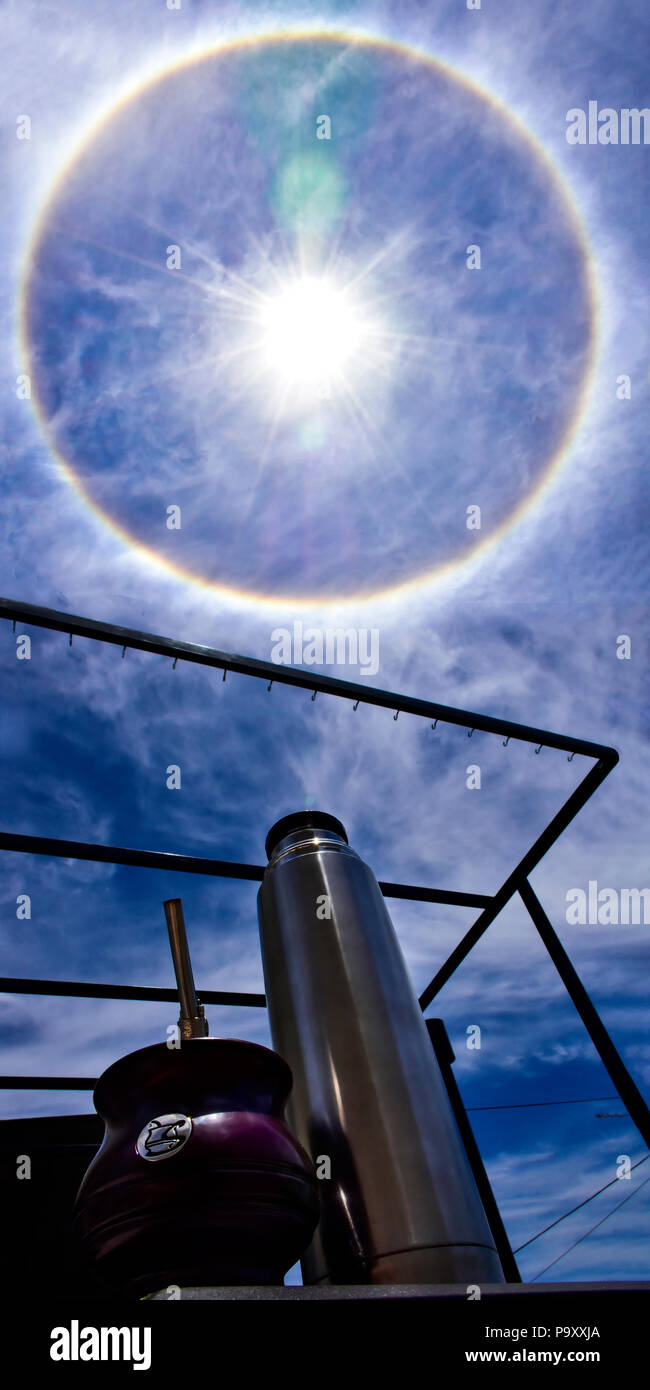 Halo solaire dans un midi d'été ensoleillé. Ciel bleu avec des nuages blancs et un halo avec les couleurs arc-en-ciel autour du soleil. Banque D'Images