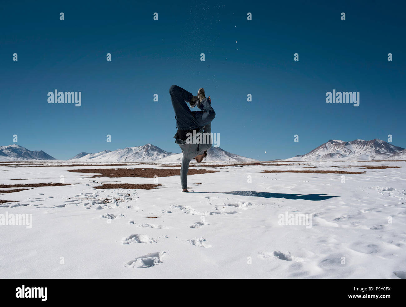 Garçon debout sur une main dans la neige (Chiguana désert avec les volcans en arrière-plan), en Bolivie. Banque D'Images