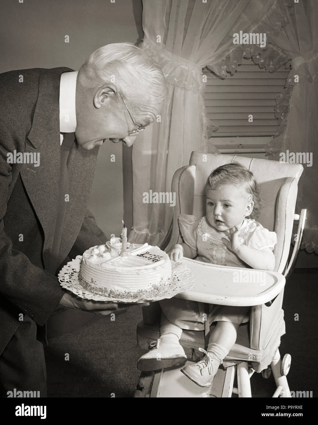 1950 Grand Pere Souriant Presentant Le Gateau D Anniversaire Avec Une Bougie A L Annee Petite Fille Assis Dans Une Chaise Haute B1321 Deb001 Hars 1 Grands Parents Grand Pere Heureux Joie Juvenile Celebration De Vie Les