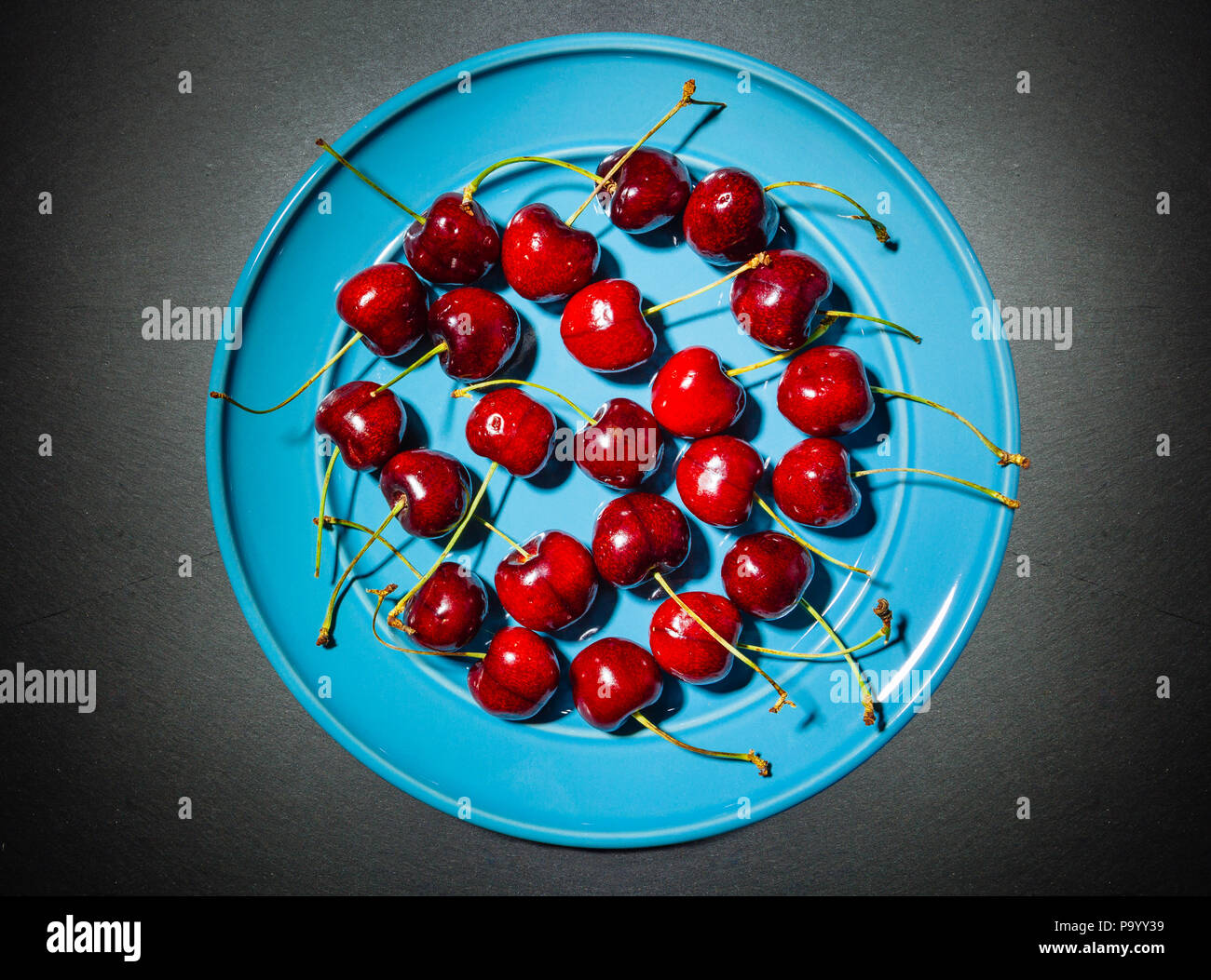 Bouquet de cerises avec tiges sur une plaque bleue, en studio, photographie alimentaire sombre Banque D'Images