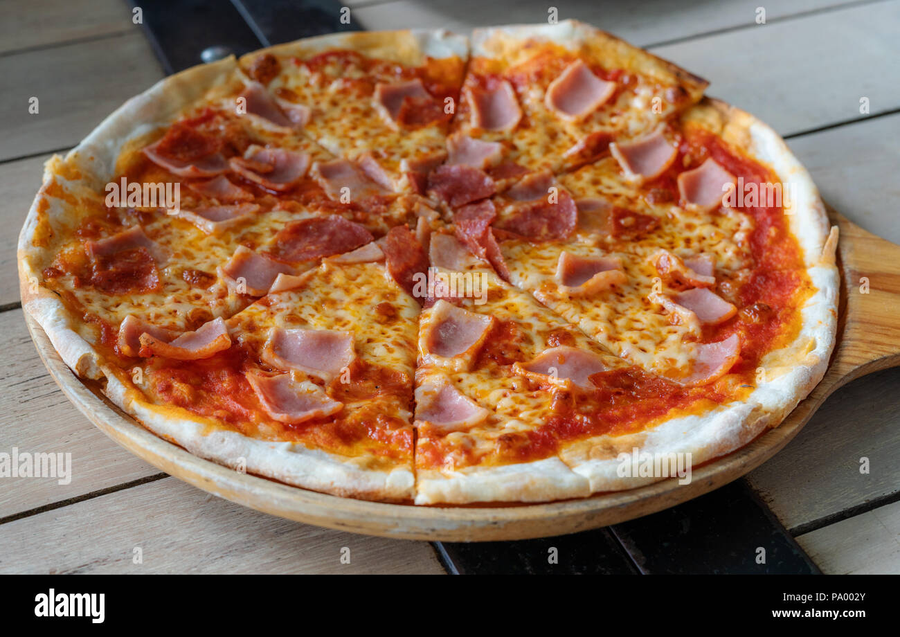 Close-up pizza jambon fromage tomate avec sources sur plateau en bois Banque D'Images