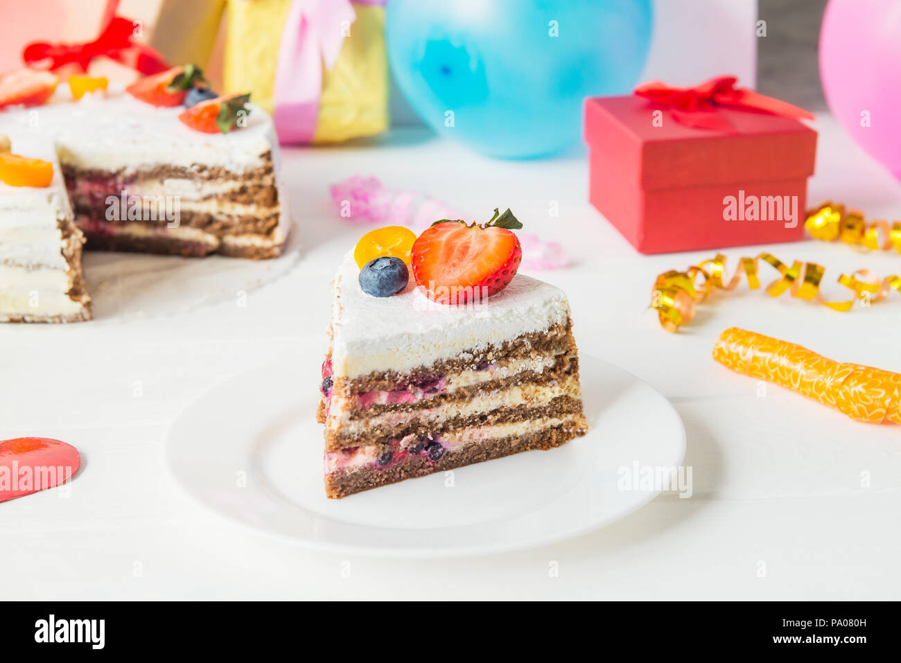 Morceau de gâteau d'anniversaire yaourts sains avec des fraises fraîches et de bleuets sur fond de fête avec partie décoration, cadeaux et ballons. Happy holi Banque D'Images