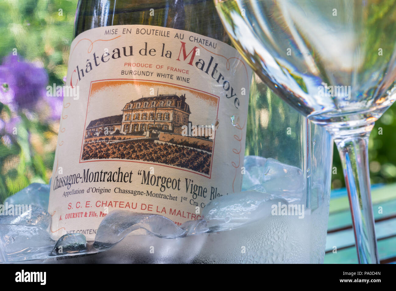 Château de la Maltroye Chassagne-Montrachet 1er cru Bourgogne blanc bouteille de vin dans un seau à glace sur la terrasse ensoleillée avec table en verre de vin France Banque D'Images