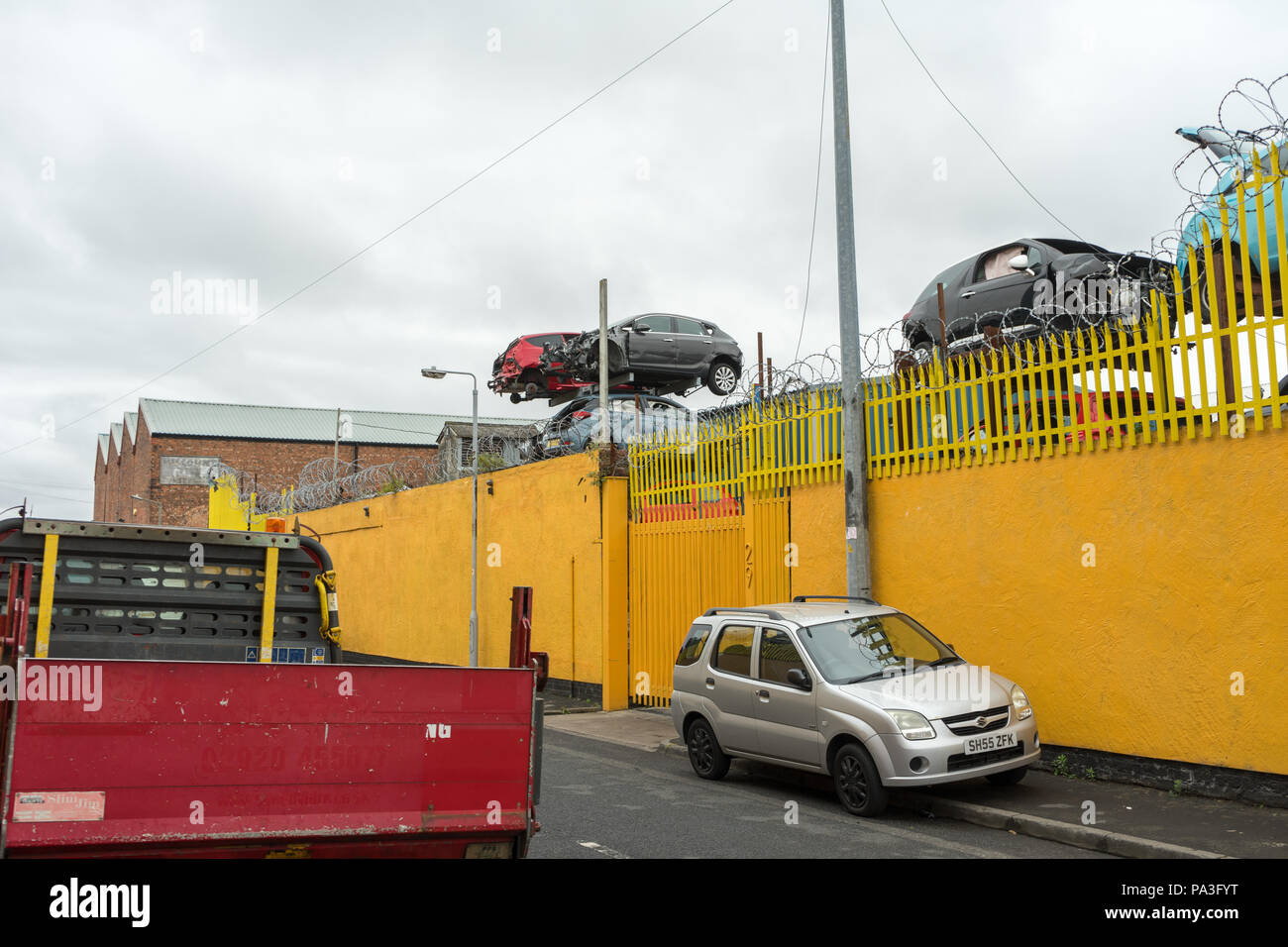 Zone industrielle à Birkenhead, Wirral, montrant un mur jaune et une voiture ferraille Banque D'Images